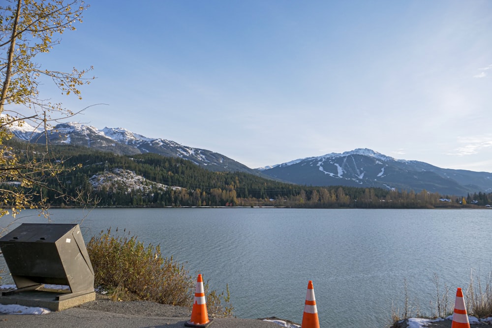 orange and white traffic cone on gray sand near lake and mountain range
