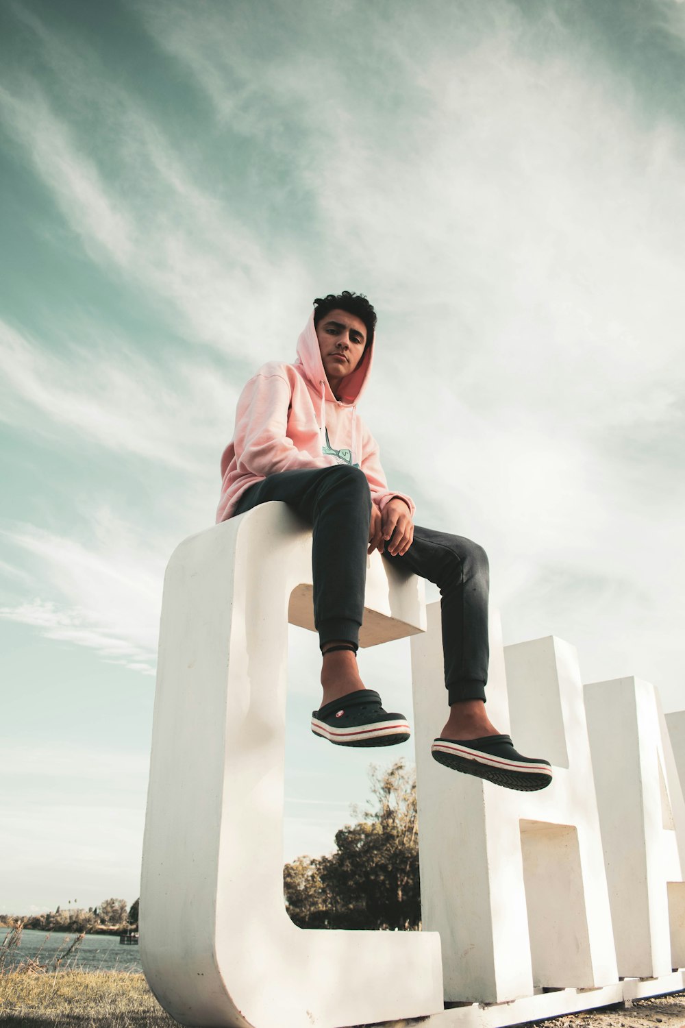 man in pink hoodie and black pants sitting on white concrete bench during daytime