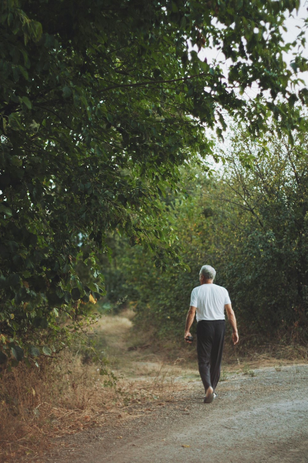 uomo in camicia bianca e pantaloni neri che cammina su strada sterrata