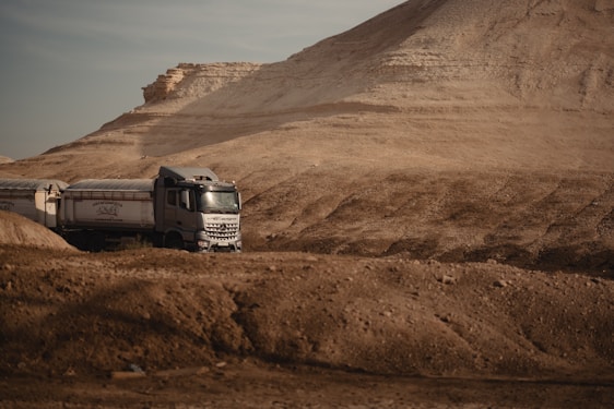 A sleek delivery truck adorned with red and black branding driving through a desert landscape under a bright sky.