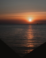 Golden sunset over the ocean with a silhouette of a cargo ship on the horizon.
