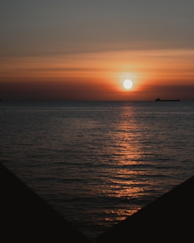 A vibrant sunset over the ocean with a cargo ship sailing calmly, symbolizing life at sea.
