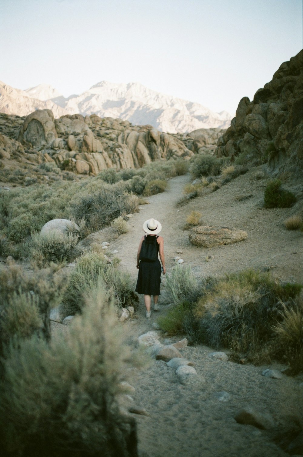 woman in black dress walking on dirt road during daytime