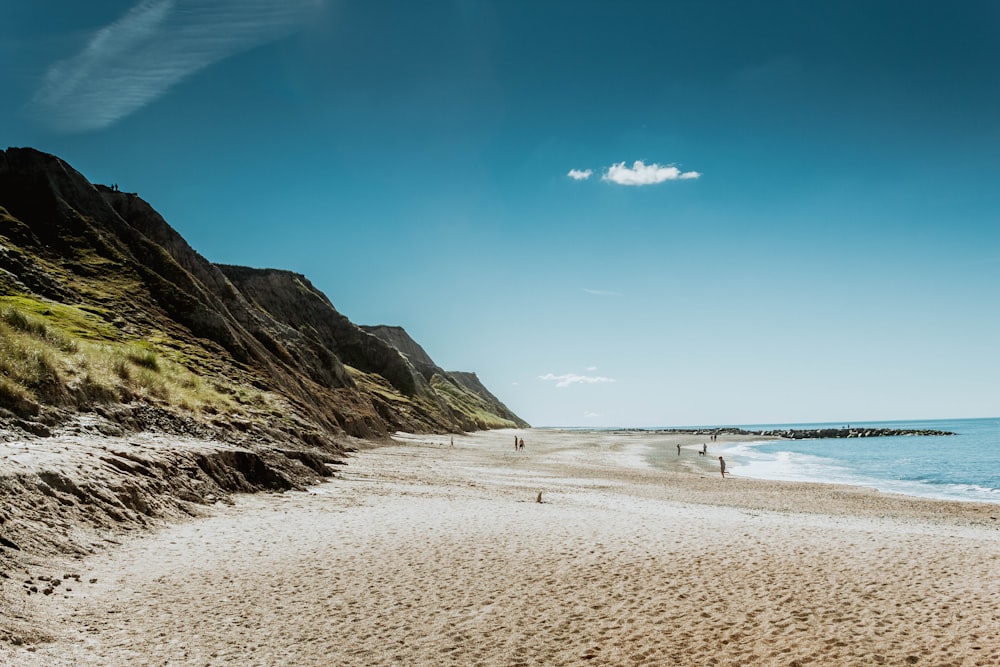 people walking on beach near mountain under blue sky during daytime