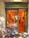 A quaint bakery storefront with a sign reading 'Martina Sweet Cakes' features a charming blue bicycle adorned with baskets of vibrant flowers parked outside. Inside, the warm glow highlights the decorative interior and pastries on display.