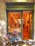 A quaint bakery storefront with a sign reading 'Martina Sweet Cakes' features a charming blue bicycle adorned with baskets of vibrant flowers parked outside. Inside, the warm glow highlights the decorative interior and pastries on display.