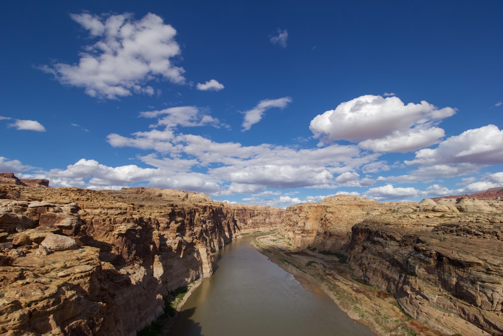 brown rocky mountain beside river under blue sky and white clouds during daytime