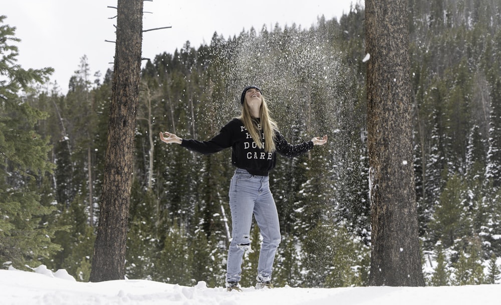 Mujer con chaqueta negra y jeans de mezclilla azul de pie en el suelo cubierto de nieve durante el día