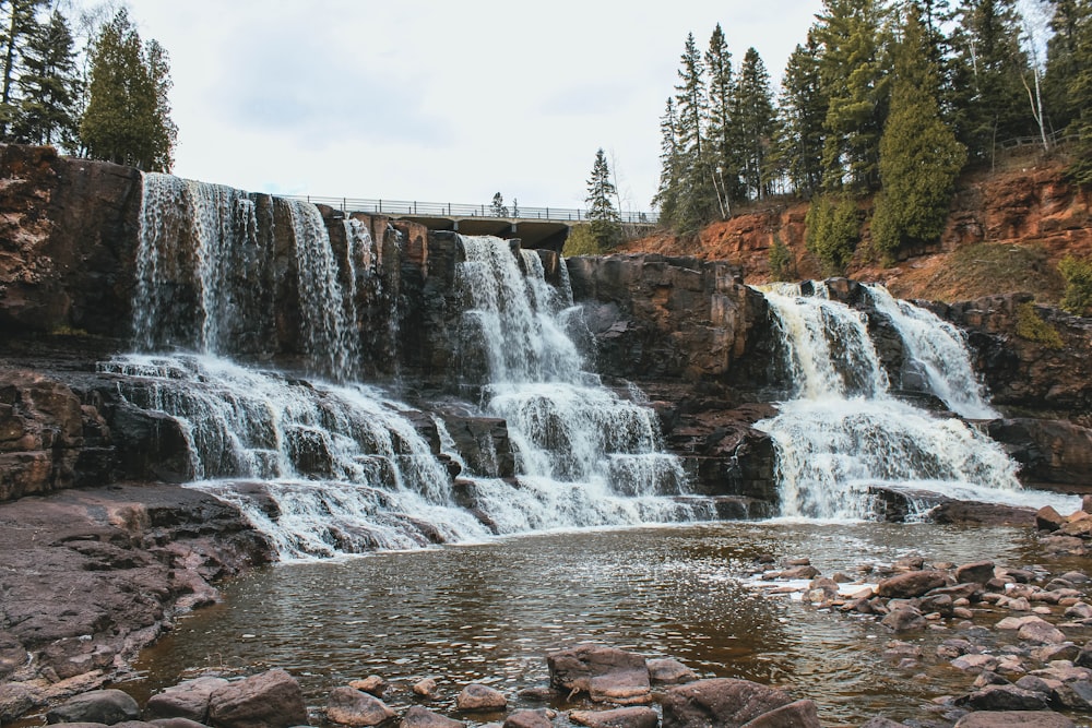 waterfalls near green trees under white sky during daytime