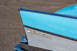A close-up of the rear section of a classic car with a distinctive tail fin design. The vibrant blue color dominates the image, complemented by chrome accents. The car's badge 'Bel Air' is prominently displayed in gold, adding a touch of elegance to the vehicle's vintage aesthetic.