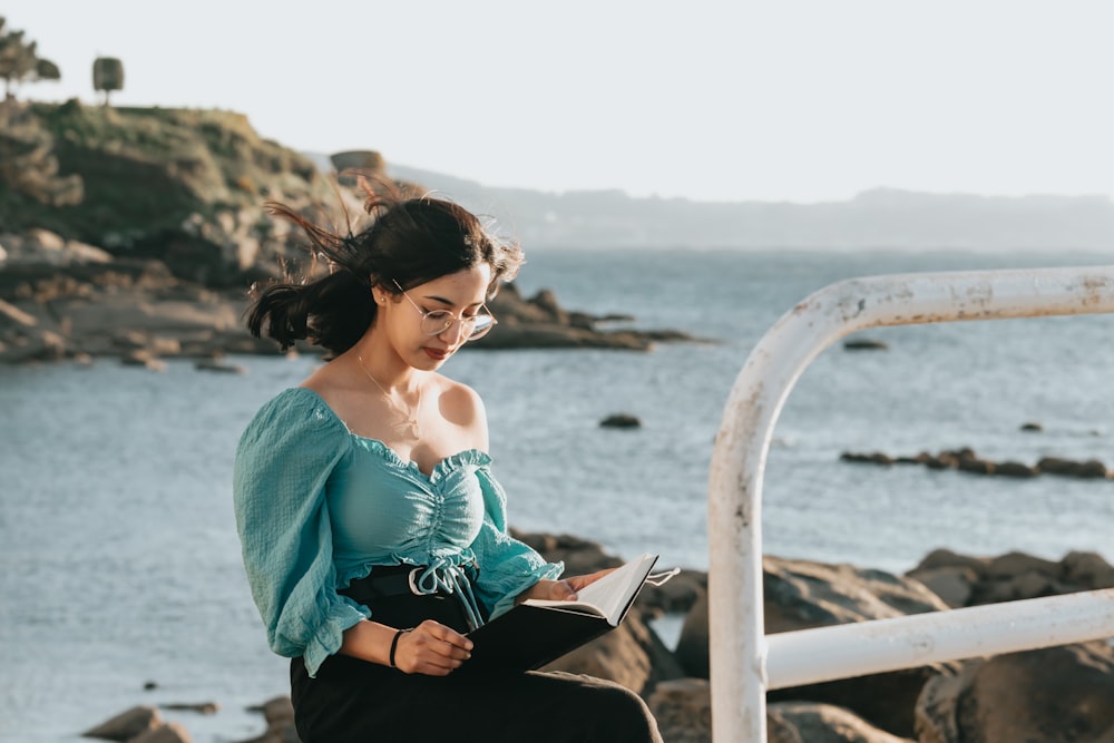 woman in teal floral dress sitting on white wooden bench during daytime