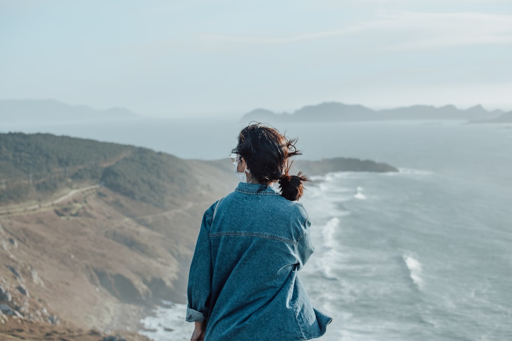 woman in blue denim jacket standing on cliff during daytime