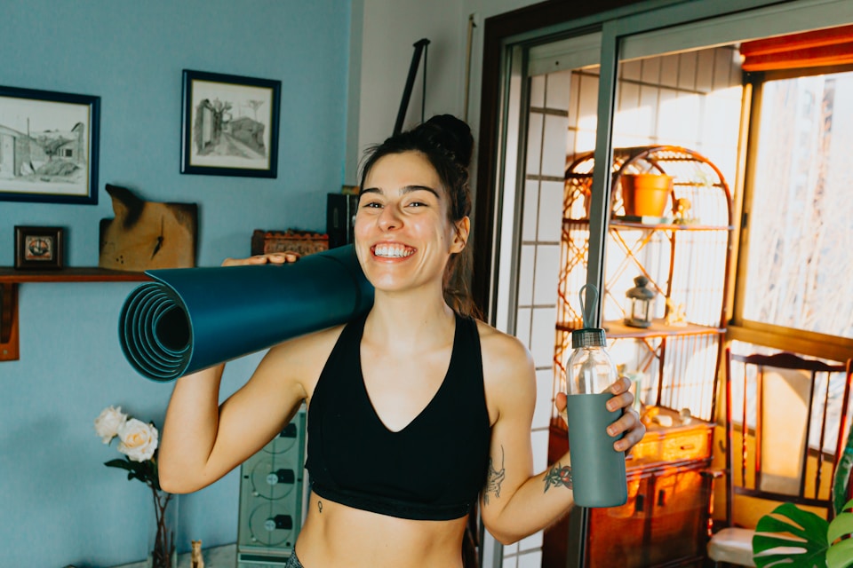 Smiling woman holding a yoga mat and water bottle, representing post-workout recovery and optimal hydration