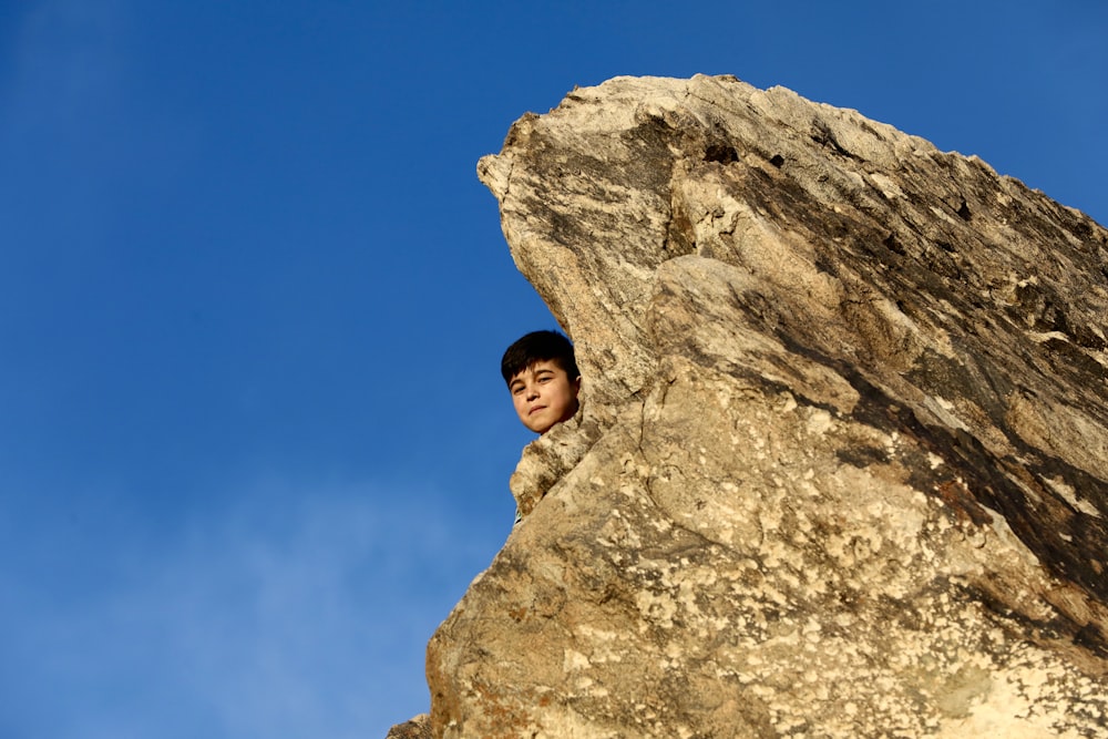 낮 동안 푸른 하늘 아래 바위 위에 서 있는 갈색 재킷을 입은 여자