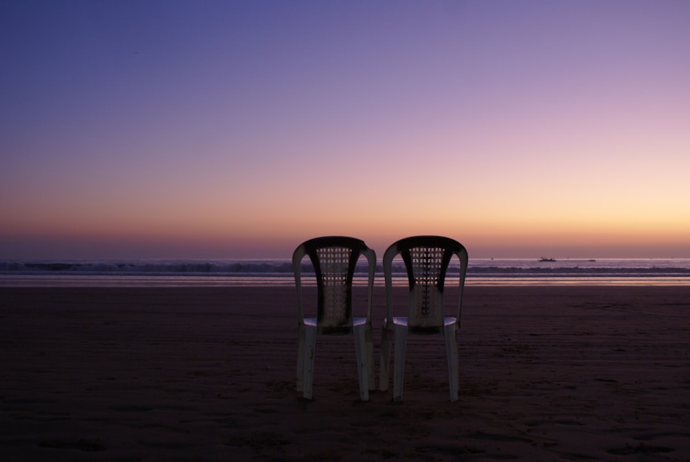 two white wooden chairs on beach during sunset