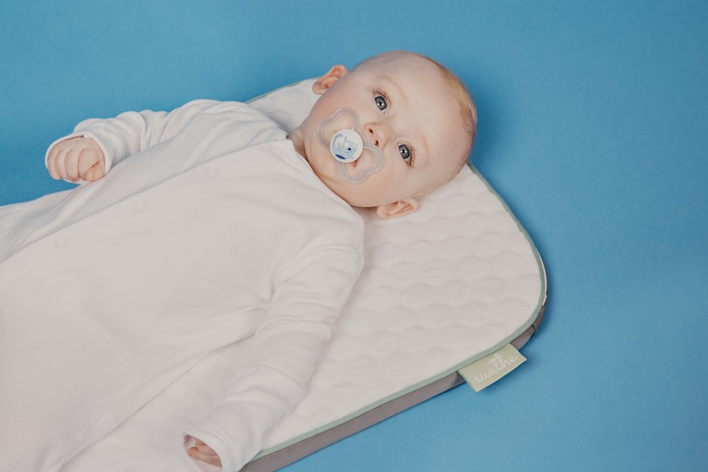 baby in white onesie lying on bed