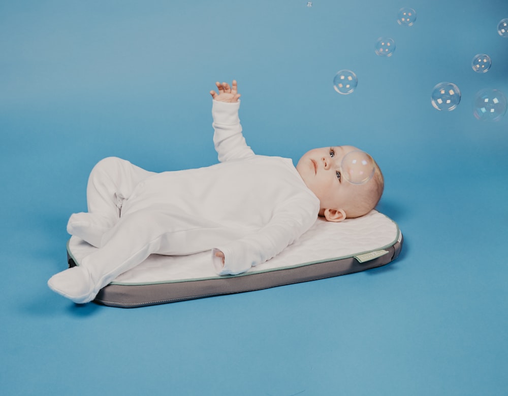 baby in white onesie lying on white bed