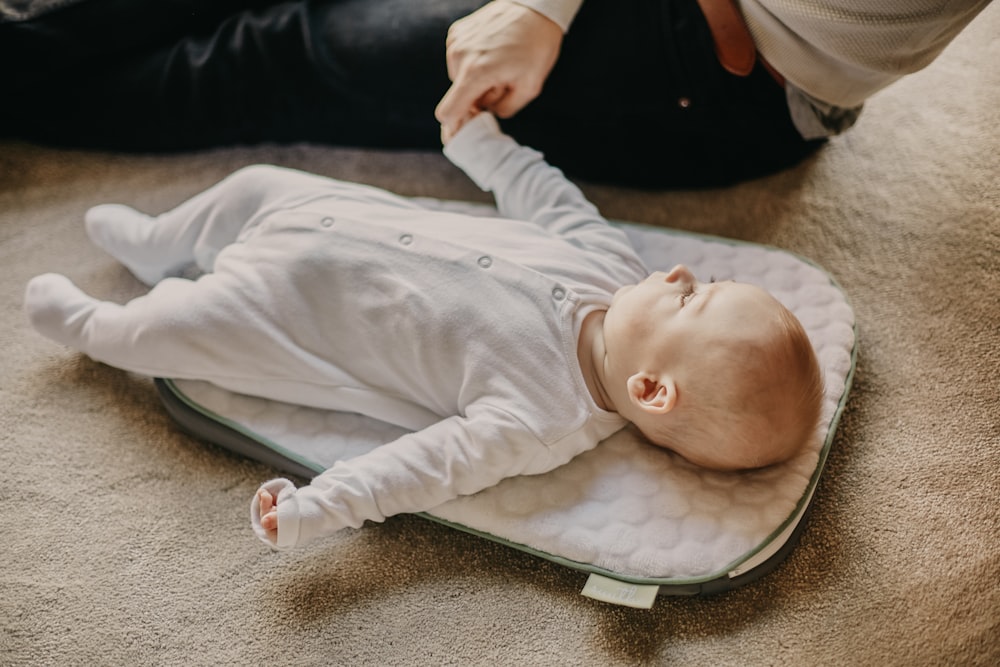 baby in white onesie lying on gray textile