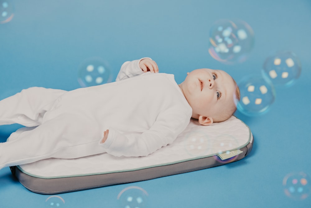 baby in white onesie lying on blue bed