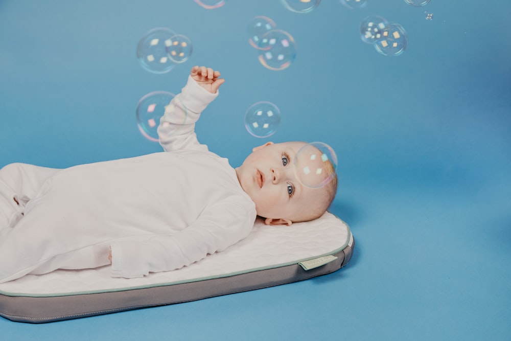 baby in white onesie lying on white bed