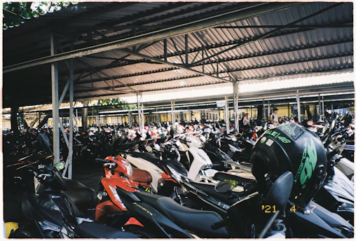 A busy parking lot showing cars, motorcycles, and bicycles neatly parked under a shaded area.