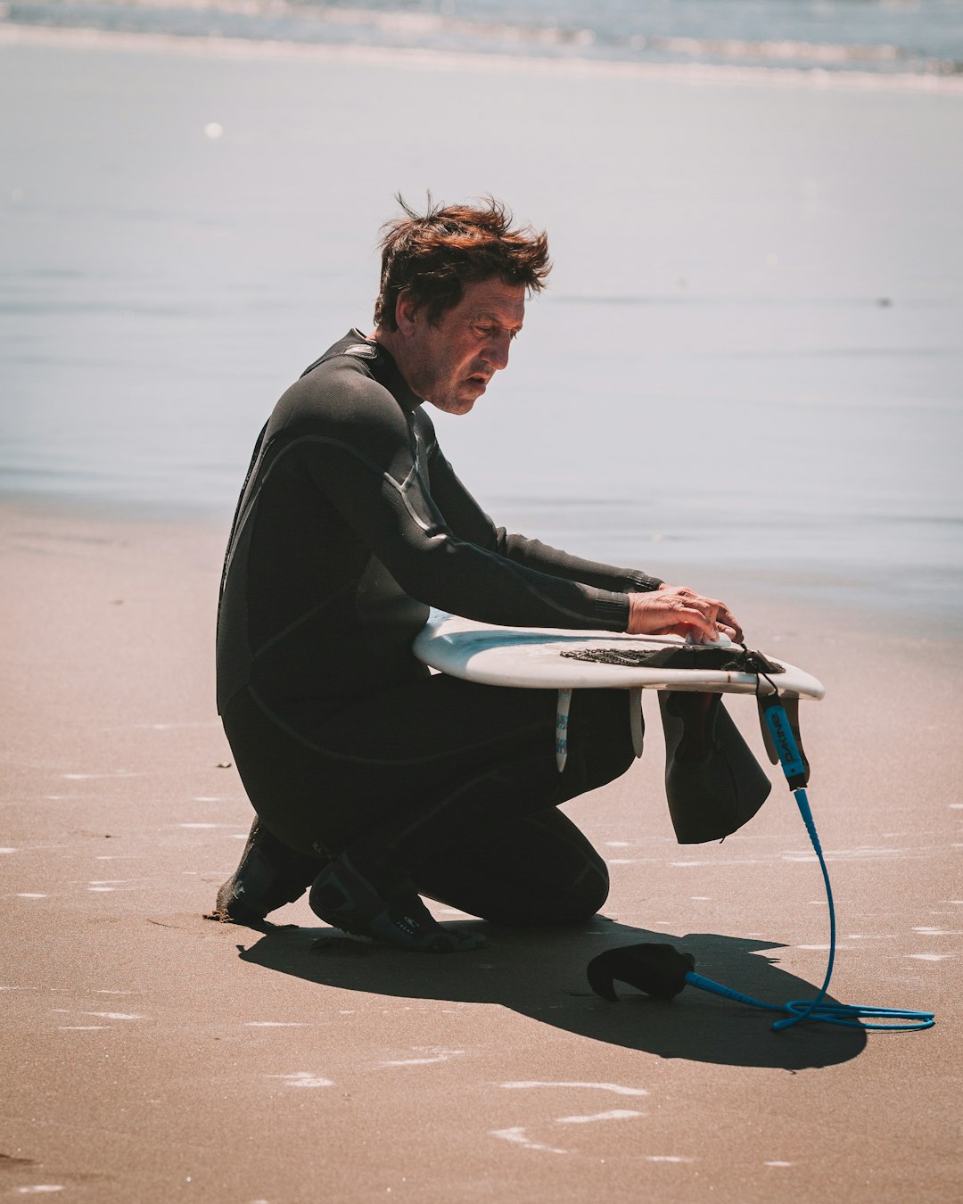 man in black leather jacket and black pants sitting on white surfboard on beach during daytime