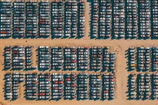Stacked used auto parts organized neatly in a large salvage yard under bright sunlight.