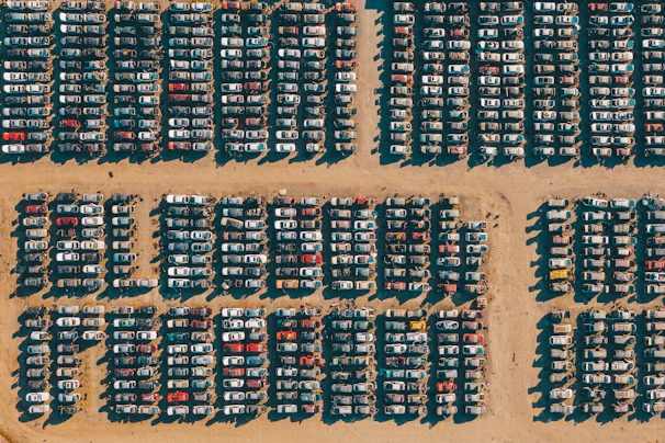 A lineup of various junk cars waiting for pickup at a sunny lot.