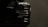 A close-up view of a black, hard-shell suitcase with a ribbed texture, partially in shadow. The suitcase appears to be sturdy, with metal rivets and reinforced edges. The lighting creates a dramatic effect, highlighting certain parts while leaving others in darkness.