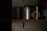 A dimly lit shelf displaying several cans of paint. The labels indicate brands such as Porter's Paints and Farrow & Ball. The cans are organized in a row, with some text partially visible due to the lighting.