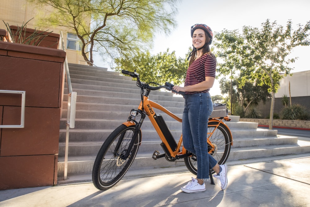 woman in white and black striped long sleeve shirt and blue denim jeans riding orange bicycle
