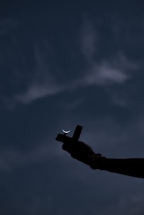 Hands gently holding a small wooden cross against a peaceful sunset background.