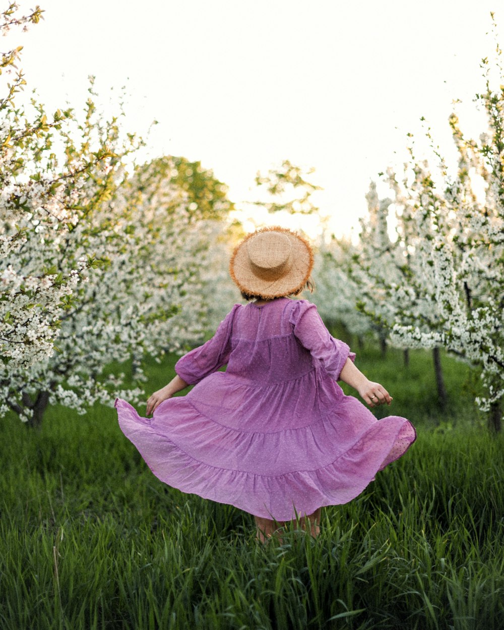 분홍색 드레스와 갈색 태양 모자를 쓴 여자가 낮 동안 푸른 잔디밭에 앉아 있다
