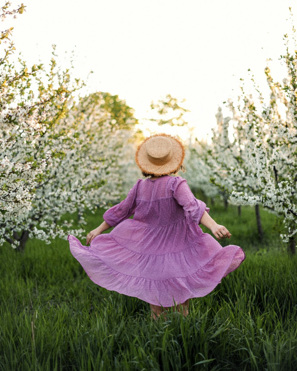 woman in pink dress and brown sun hat sitting on green grass field during daytime