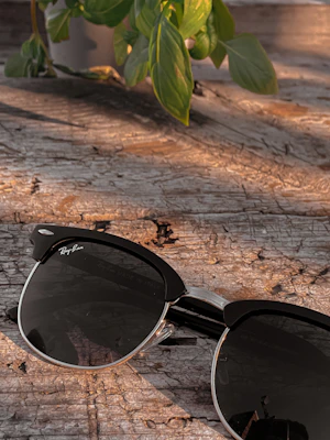 Close-up of trendy sunglasses resting on a wooden table with sunlight filtering through leaves.