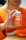 A person is holding a bottle of turmeric and ginger gummies labeled 'Jellybee' with an orange flavor. The person is wearing an orange sweater, and their hands are prominently visible, gently clutching the bottle. The background is slightly blurred.