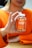 A person is holding a bottle of turmeric and ginger gummies labeled 'Jellybee' with an orange flavor. The person is wearing an orange sweater, and their hands are prominently visible, gently clutching the bottle. The background is slightly blurred.