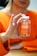 A person is holding a bottle of turmeric and ginger gummies labeled 'Jellybee' with an orange flavor. The person is wearing an orange sweater, and their hands are prominently visible, gently clutching the bottle. The background is slightly blurred.