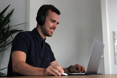 A senior man using a laptop with headphones, focused on an educational guide.