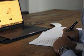 A person reviewing a resume on a laptop with a notepad and pen nearby.