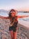 woman in black tank top and black shorts wearing black sun hat standing on beach shore
