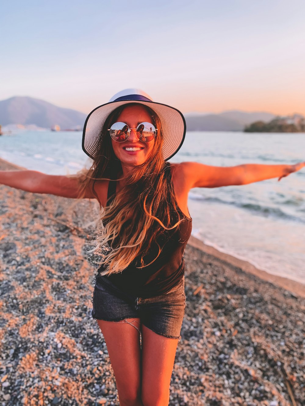 Femme en débardeur noir et short noir portant un chapeau de soleil noir debout sur le rivage de la plage