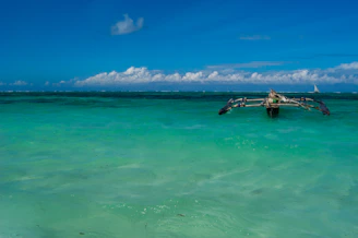 A vibrant outrigger boat gliding over crystal-clear turquoise waters near lush Caramoan islands under a bright blue sky.