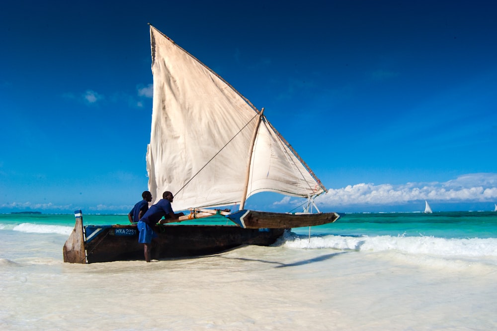 man in black shirt sitting on white and brown sail boat on sea shore during daytime