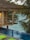 A tranquil scene of a wooden cabin with a thatched roof overlooking an infinity pool. The setting is surrounded by lush palm trees with a view out to a calm, blue sea. The warm glow from a lamp inside the cabin adds a cozy ambiance.