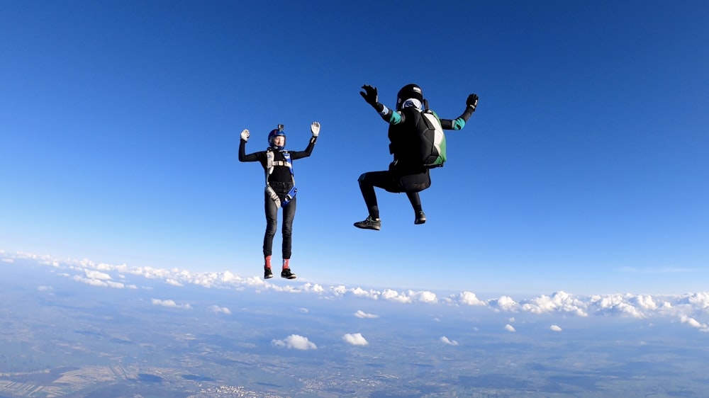 2 femmes en veste et pantalon noirs sautant sur des nuages blancs pendant la journée