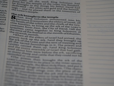 A close-up shot of a page in a book features a biblical text with visible chapter and verse numbers. The text discusses King Solomon and the ark being brought to the temple, with various small headings in bold. On the right side, there are empty lines for notes.