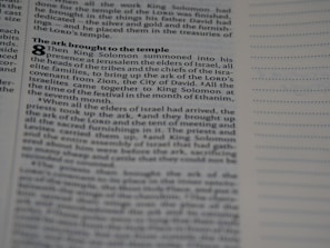A close-up shot of a page in a book features a biblical text with visible chapter and verse numbers. The text discusses King Solomon and the ark being brought to the temple, with various small headings in bold. On the right side, there are empty lines for notes.