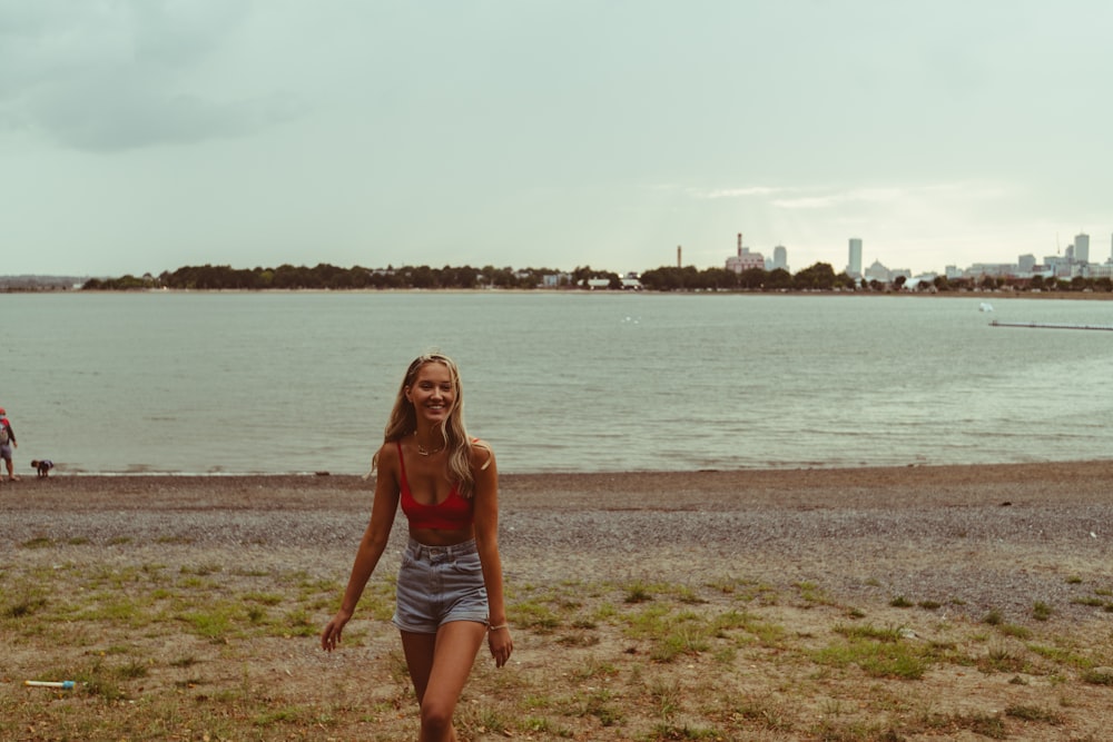 woman in red tank top and blue denim shorts sitting on brown grass field near body