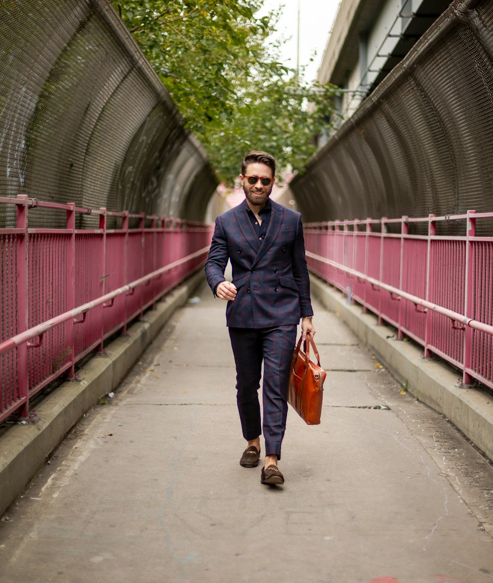 homme en veste noire et jeans en denim bleu tenant un sac fourre-tout orange